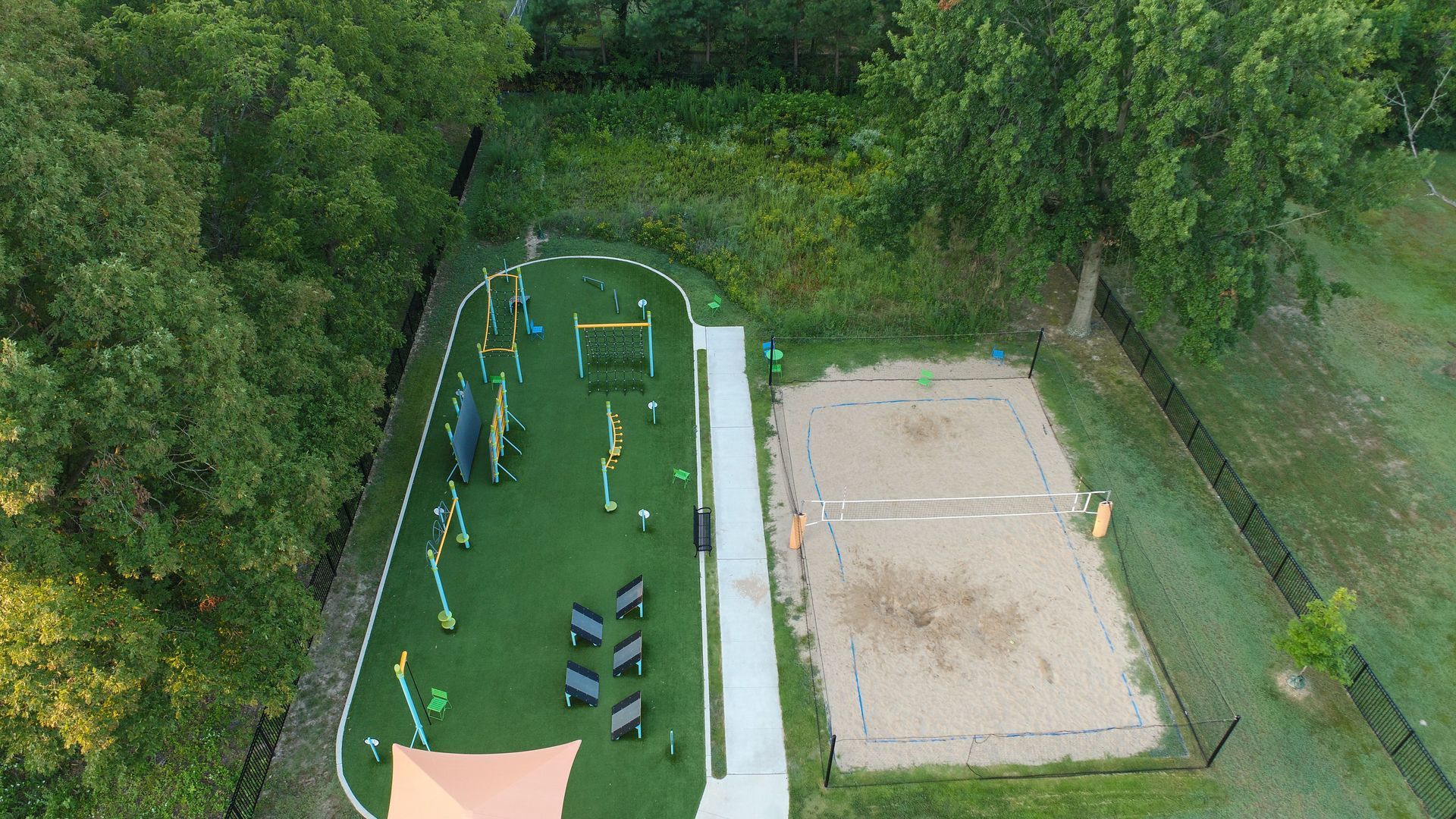 Aerial view of a dog park with agility equipment on green turf and a sand volleyball court.
