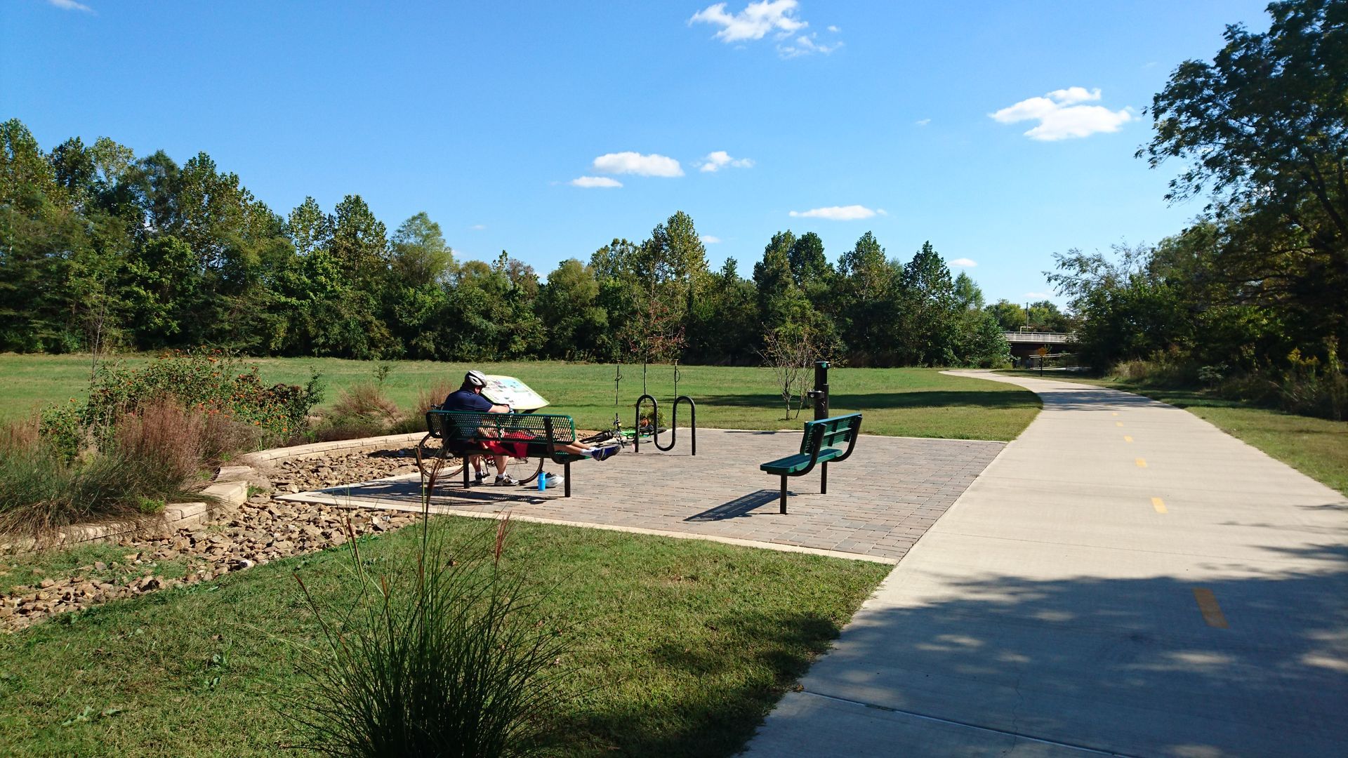 Park exercise area with equipment near a paved path and green space.