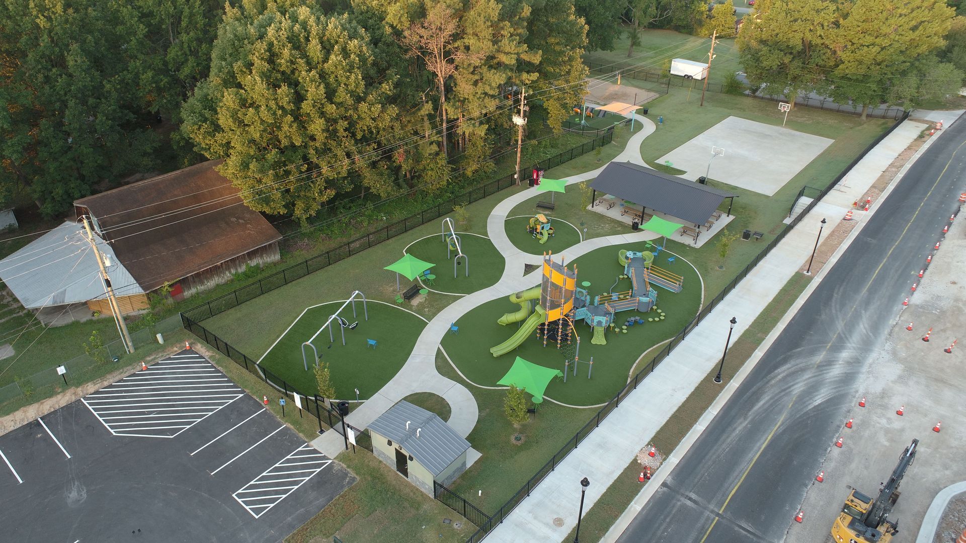 Aerial view of a playground with play structures, a pavilion, and a pathway, all behind a fence.