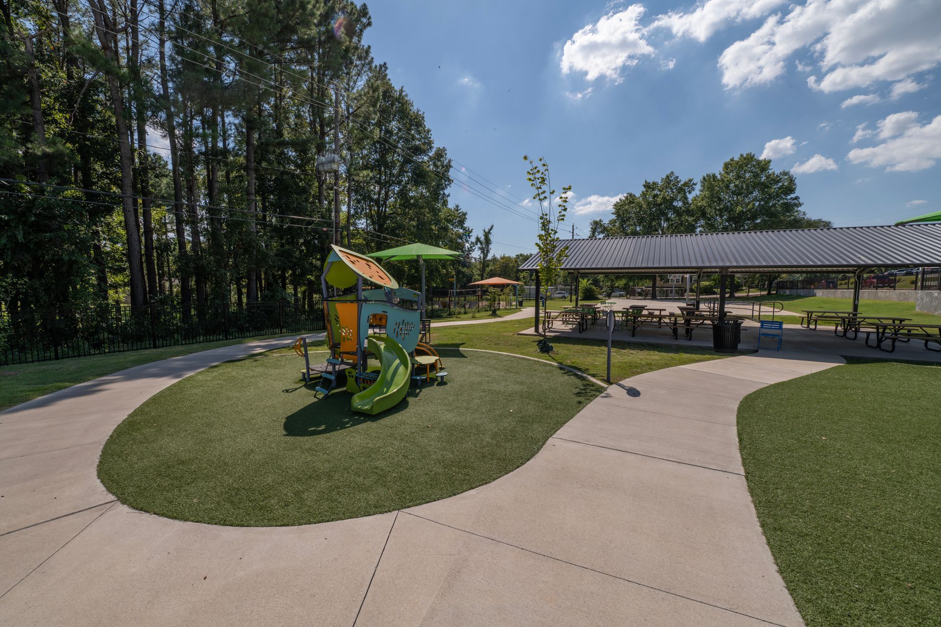 A playground with a slide, shelter with picnic tables, and trees on a sunny day.