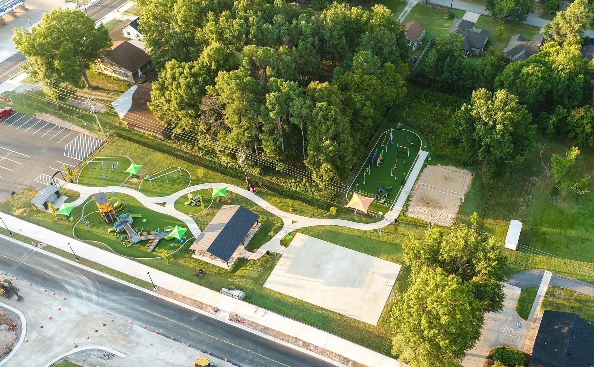Aerial view of a park with playground, sports field, and trees. Concrete pathways and structures are visible.