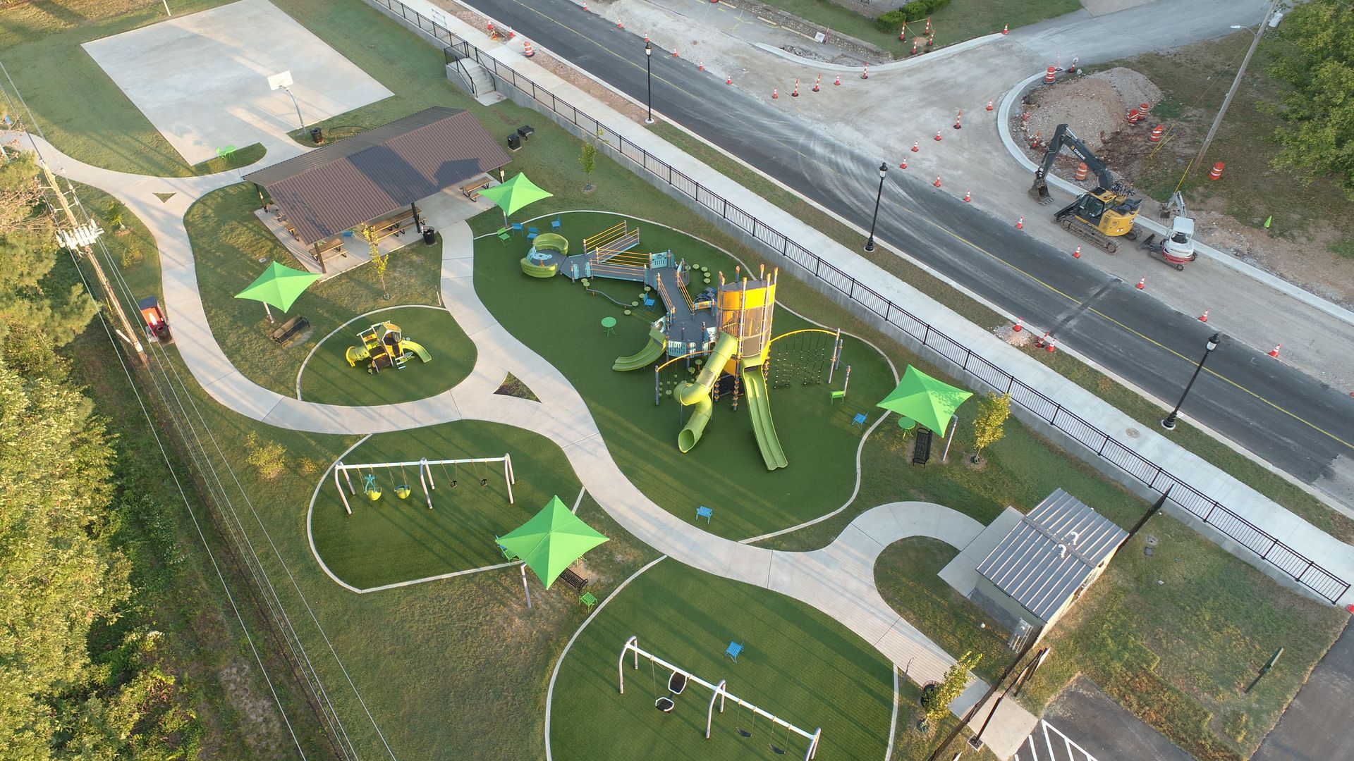 Aerial view of a playground with green structures, walkways, shade canopies, and a basketball court.