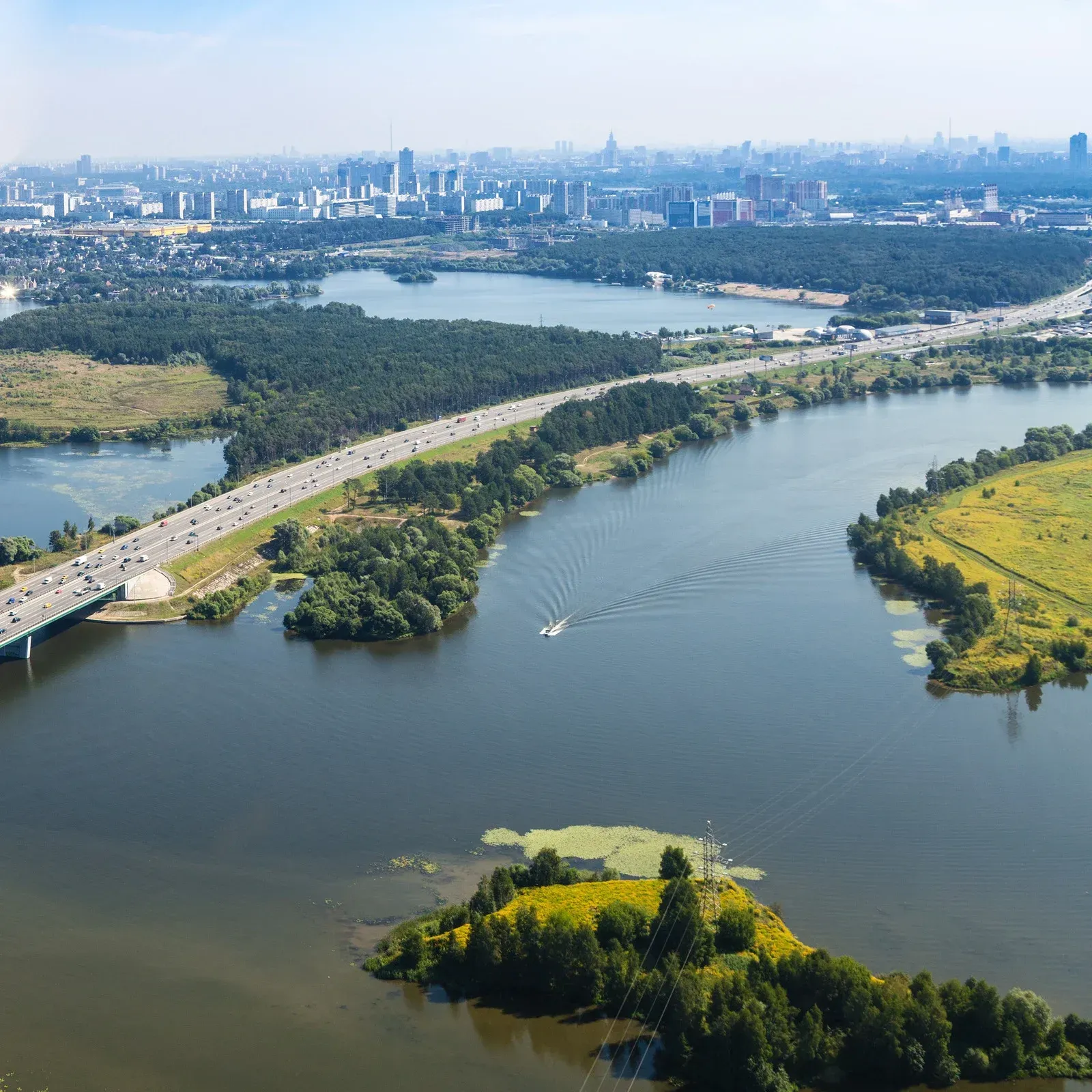 Scenic aerial view of a river with a highway bridge, small islands, and a distant cityscape under a blue sky.