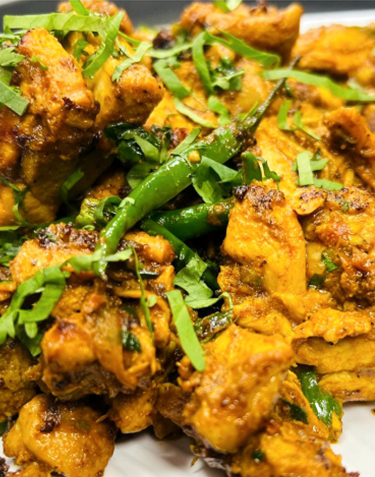 Close-up of golden-brown fried chicken pieces with green chilies and chopped cilantro.