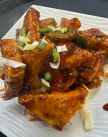 Fried paneer in red sauce with bell peppers and green onions.