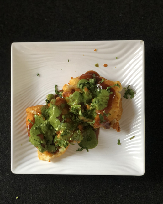 Fried food with green sauce and red sauce, on a white square plate, black background.