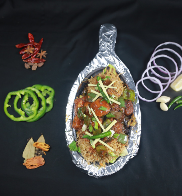 Sizzling dish with vegetables and rice, garnished with green onions and peppers, served on a foil-lined platter.