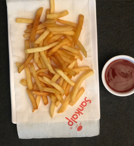 Golden french fries on a white napkin next to a small bowl of red ketchup.