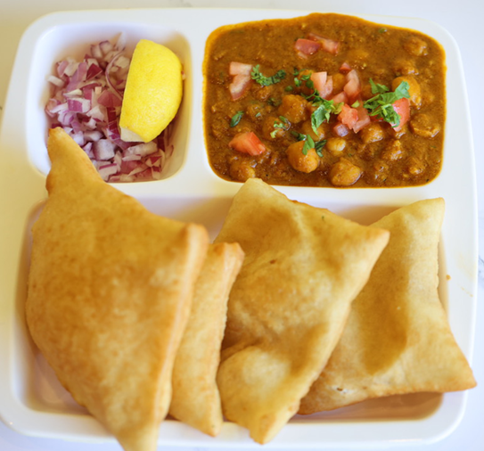 Plate of Indian food: fried samosas, chickpea curry, chopped onions, and lemon wedge.