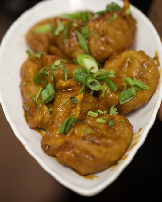 Dumplings in a white dish, glazed with sauce, garnished with green onions.