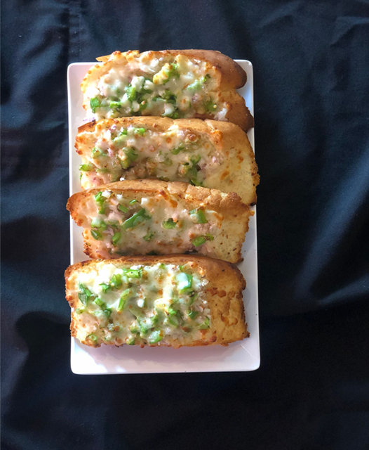 Four slices of garlic bread topped with melted cheese and green peppers on a white plate.