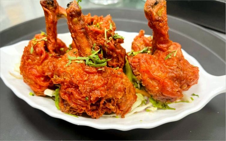 Plate of fried chicken drumsticks, reddish-brown, garnished with herbs, on a white plate.