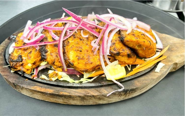 Sizzling Indian paneer dish with red onions, served on a wooden plate.