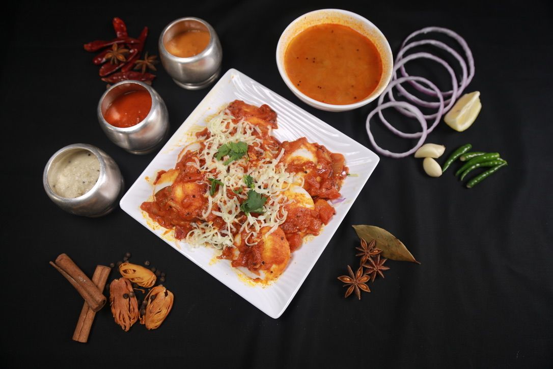 Paneer dish with sauce, onions, spices, and garnishes on a black surface.