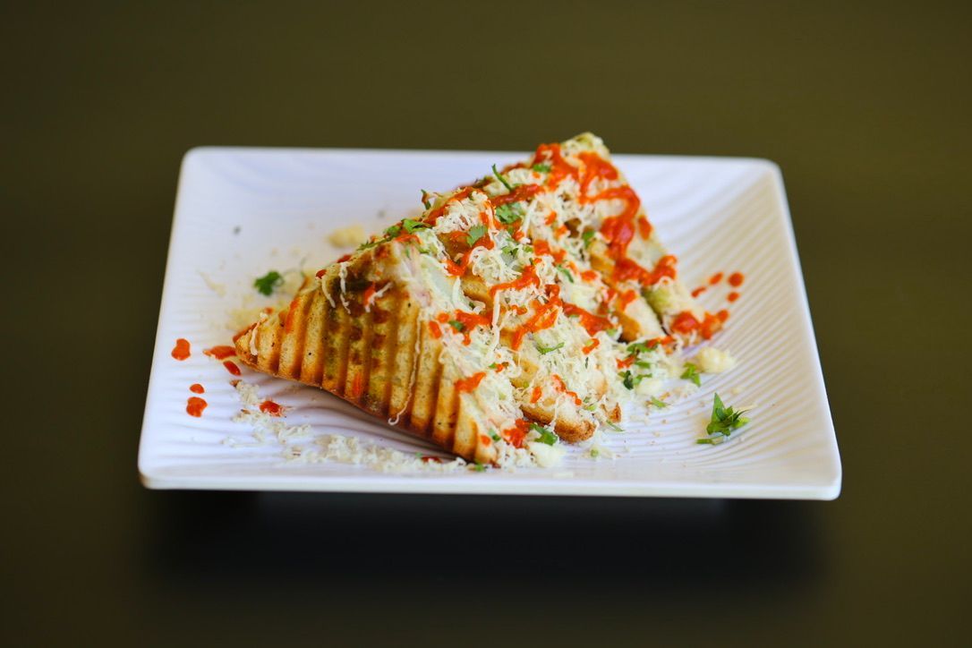 Grilled cheese sandwich on a white plate, drizzled with red sauce and sprinkled with herbs.
