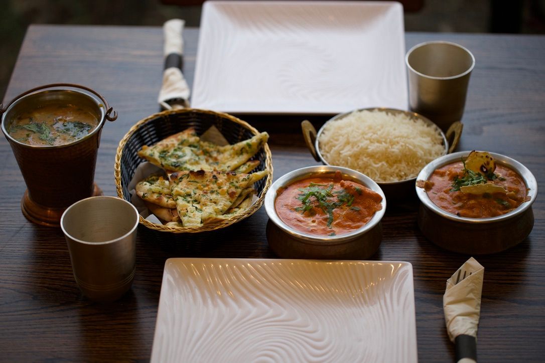 Indian food spread on a wooden table, featuring bowls of curry, rice, naan bread, and drinks.