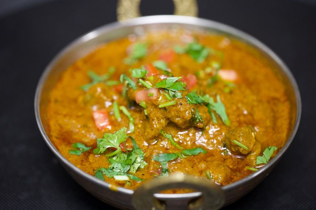 Close-up of a bowl of curry, orange sauce, with pieces of meat, garnished with cilantro and tomatoes.