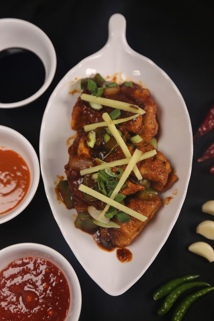 Fried tofu dish with sauce, garnished with ginger and scallions, served with dipping sauces.