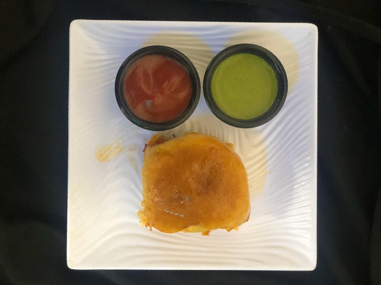 A plate with a sandwich and two small bowls of red and green sauces.