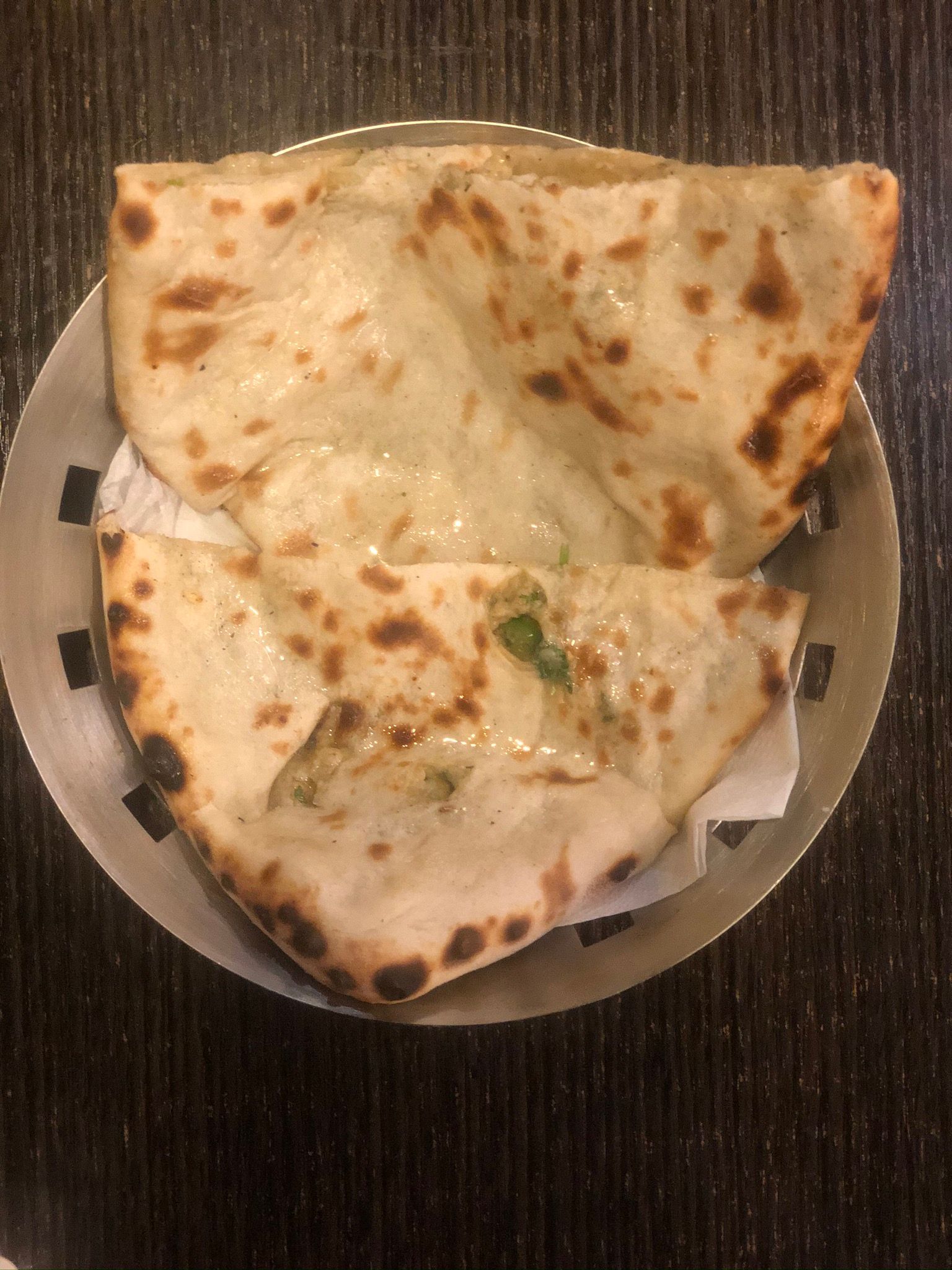 Two pieces of naan bread on a round, woven basket; golden-brown edges.