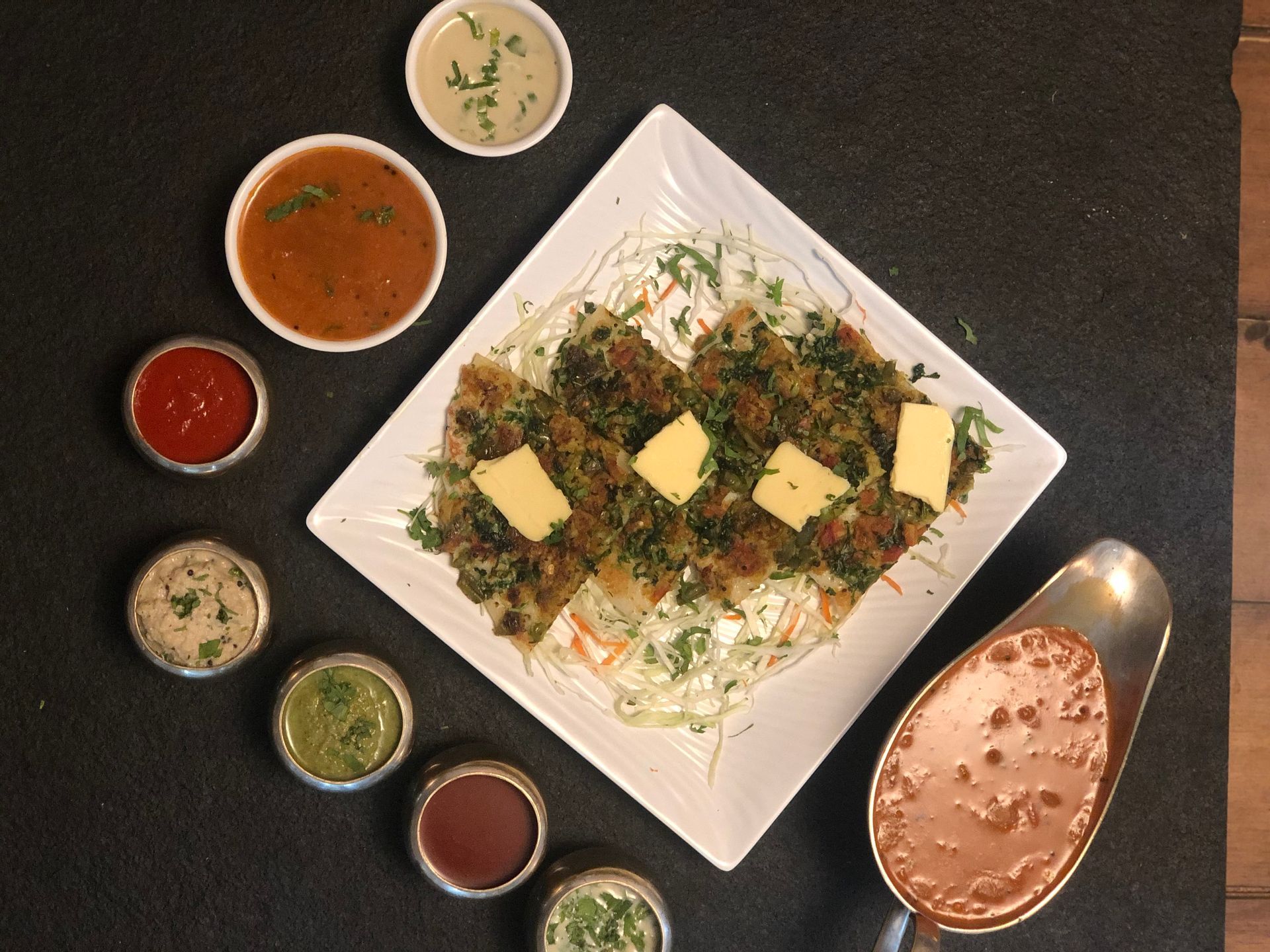 Close-up of a plate with food, surrounded by small bowls of sauces, and a serving dish with more sauce.