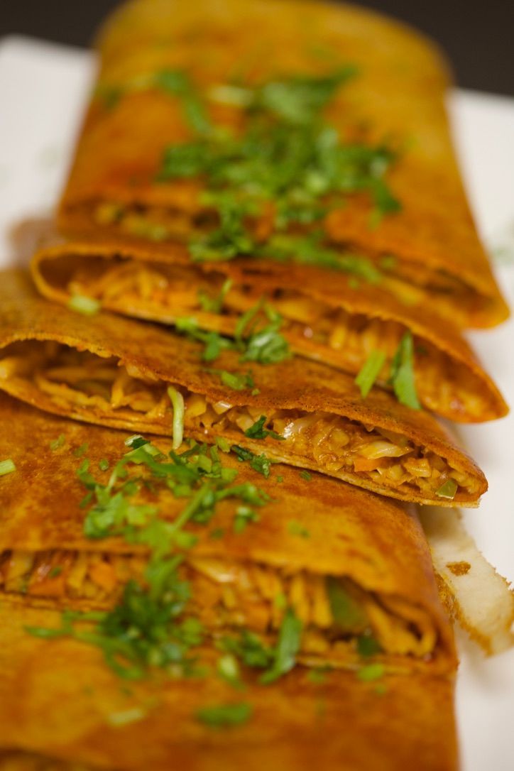 Sliced, golden-brown dosa filled with visible savory filling, garnished with chopped green herbs.