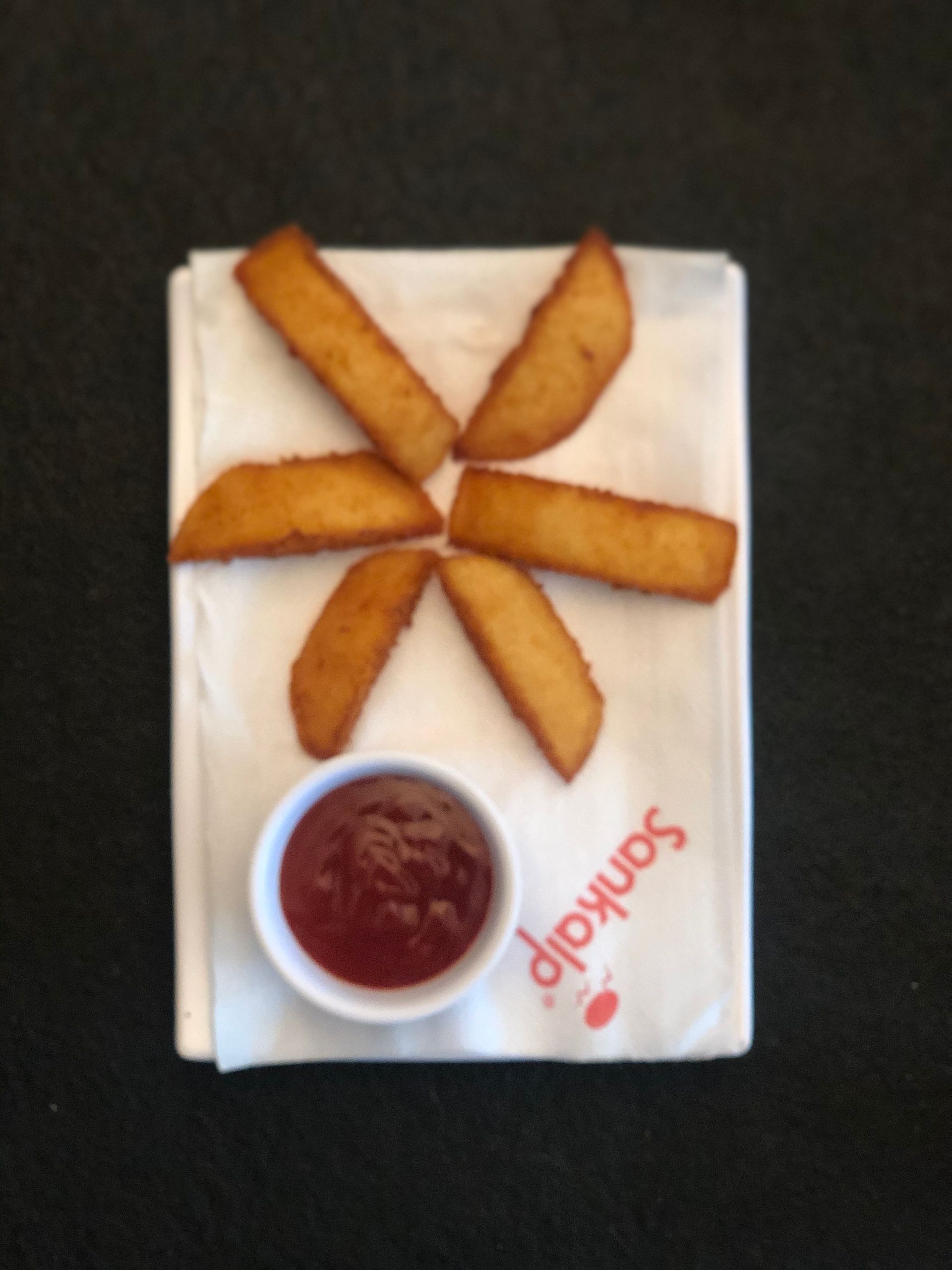 Potato wedges arranged like a star on a white napkin, with a small bowl of red sauce beside them.