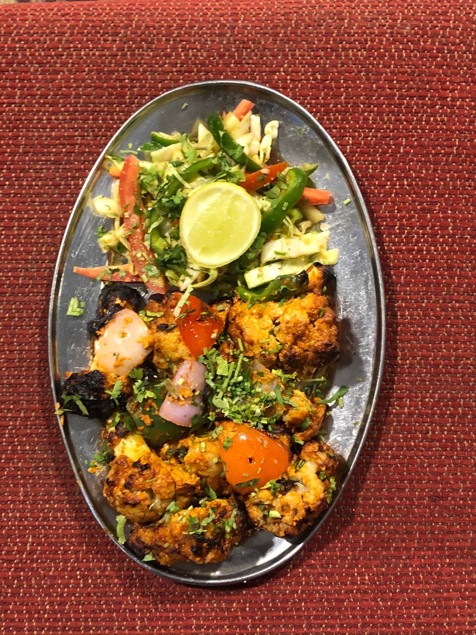 Plate of Indian food, including fried cauliflower, peppers, onions, tomatoes, and a side salad.