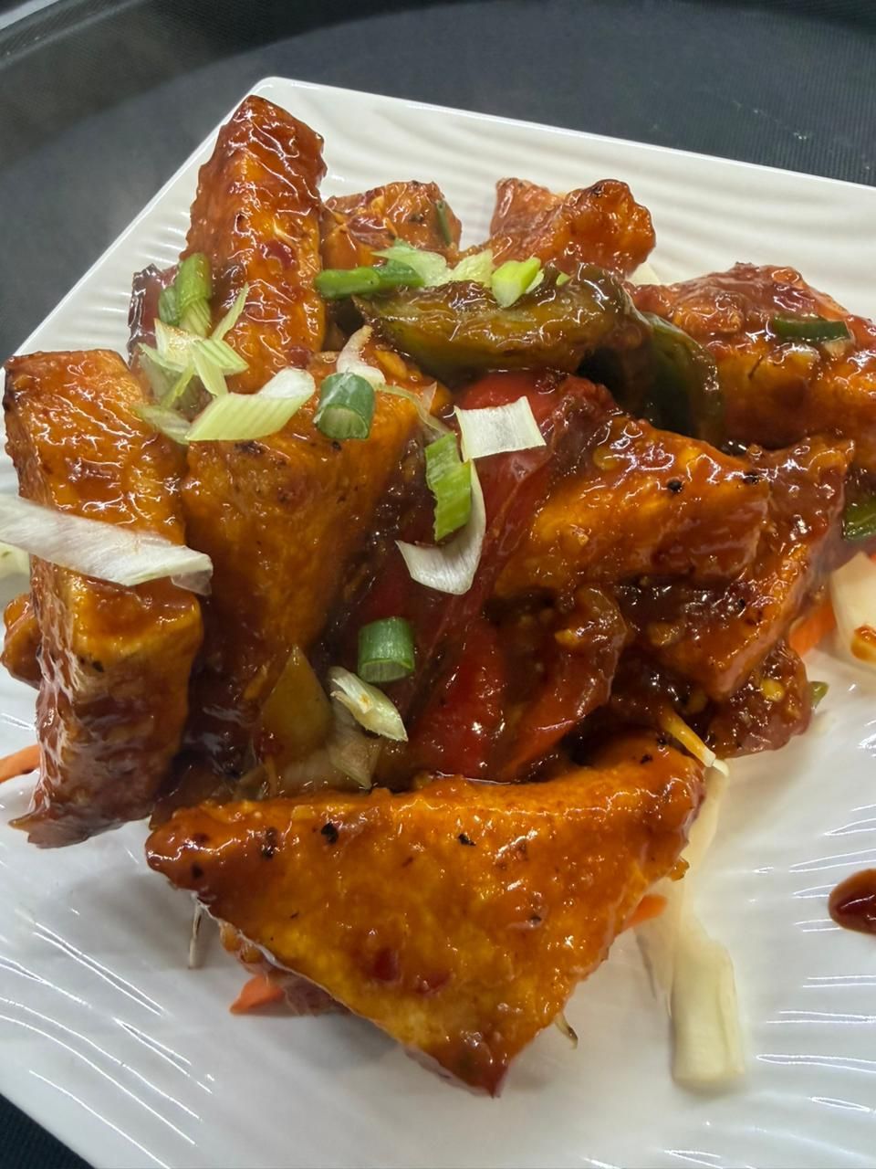 Fried tofu with peppers and scallions on a white plate.
