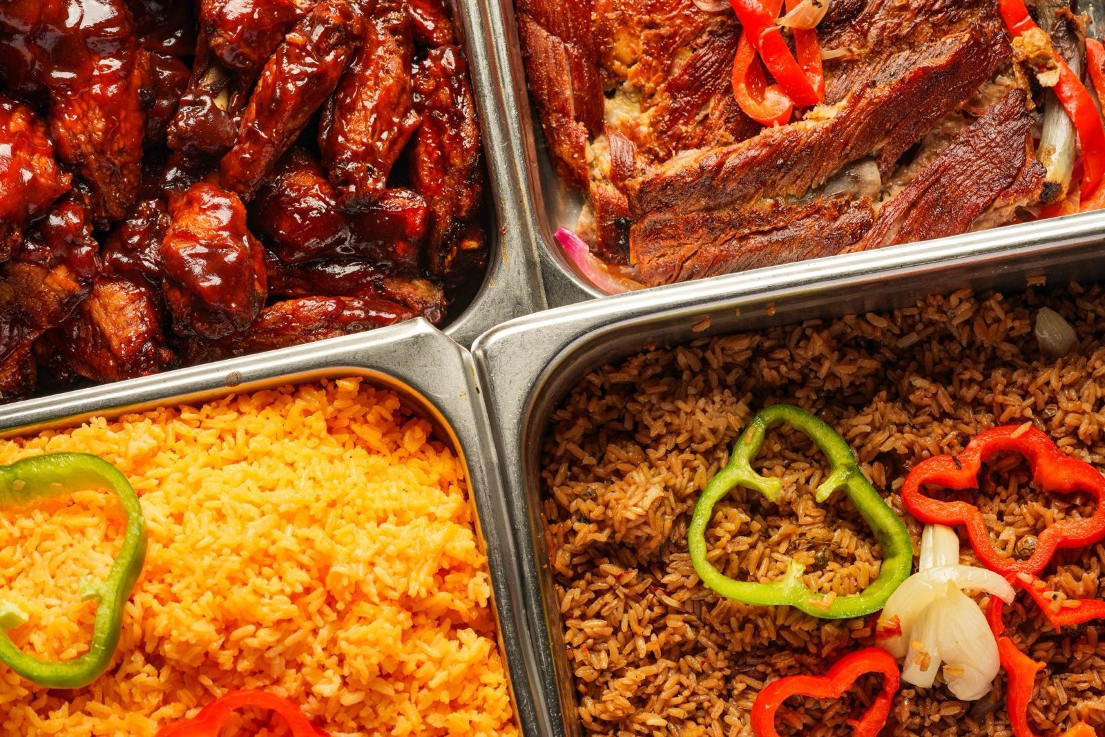 Food trays with BBQ chicken wings, roasted meat, yellow rice, and brown rice with peppers.