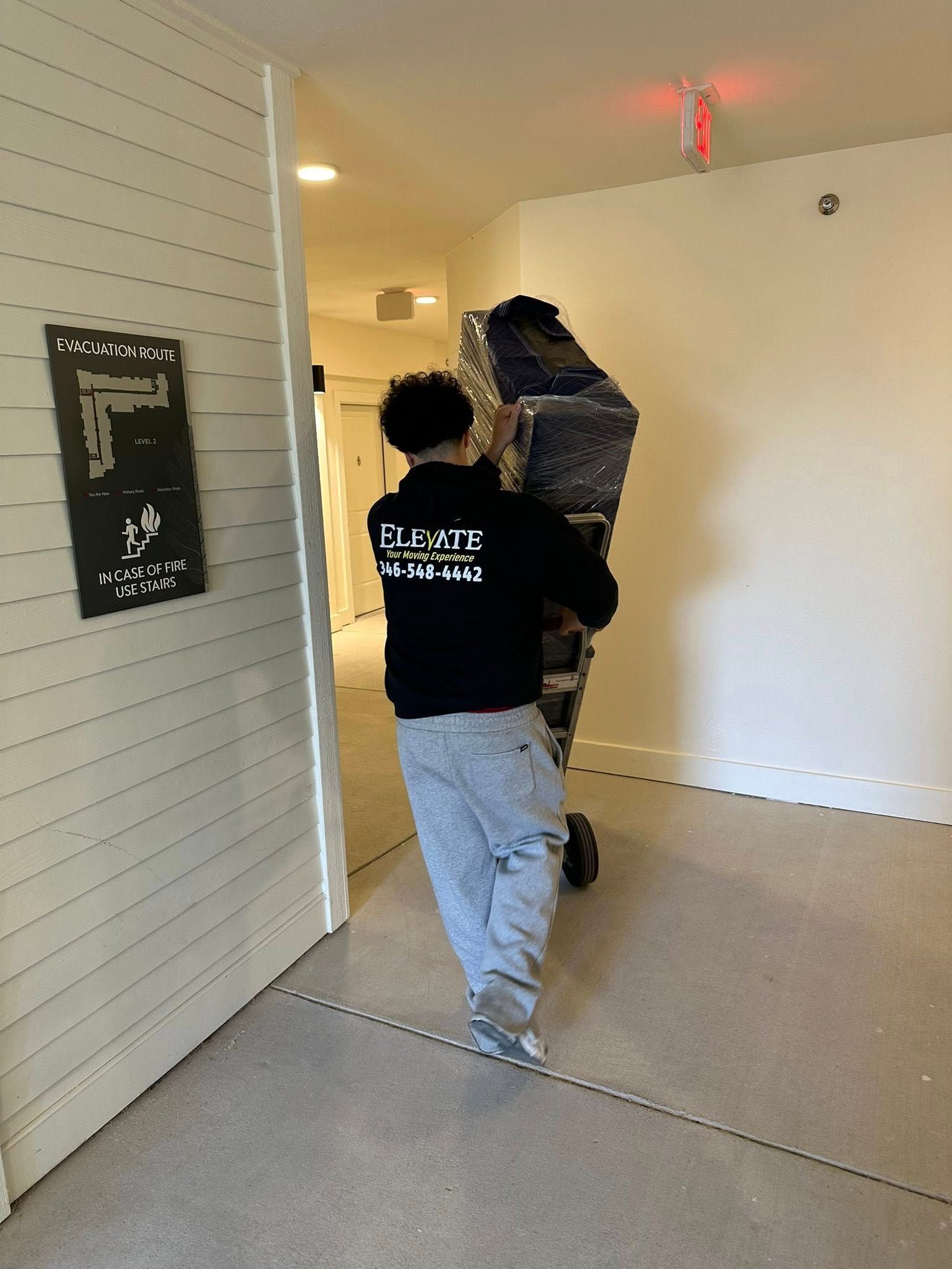 Person carrying a wrapped piece of furniture through a doorway. Hallway with beige walls and a light.
