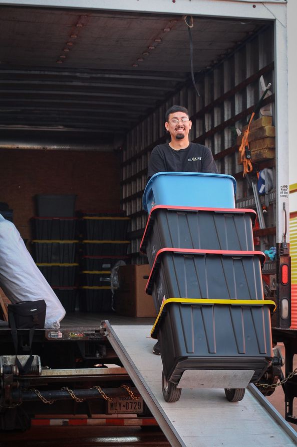 Man pushing stack of storage bins down a ramp from a truck. Bins are black and blue.
