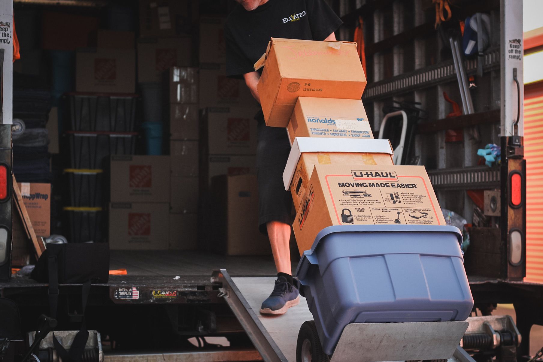 Man loading boxes onto a hand truck from a truck ramp. Storage unit interior.