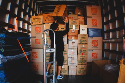 Person stacking boxes in a truck, using a ladder. Many cardboard boxes fill the truck's interior.