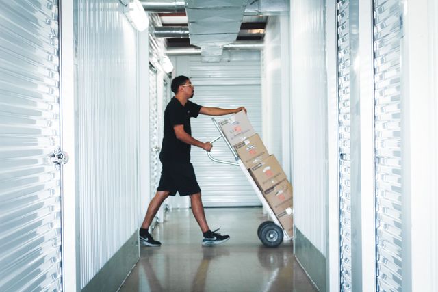 Person pushing boxes on a dolly down a storage unit hallway.