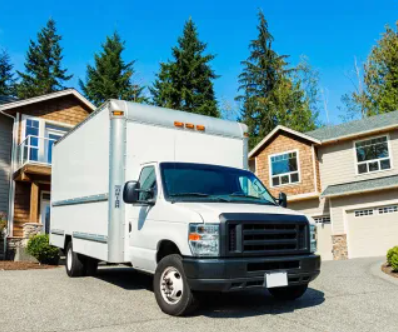 White box truck parked in a suburban driveway in front of a house under a clear blue sky