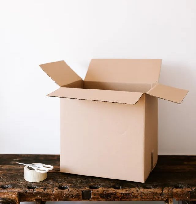 Opened cardboard box on a wood table, tape and scissors next to it.