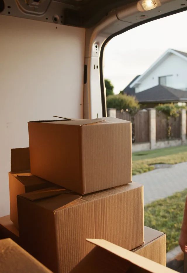 Cardboard boxes stacked inside a van, with a house visible through the open back door.