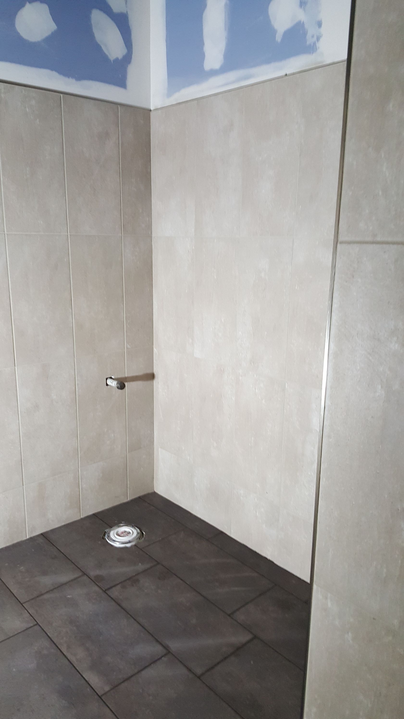 Shower stall under construction; tan tile walls, dark tile floor.
