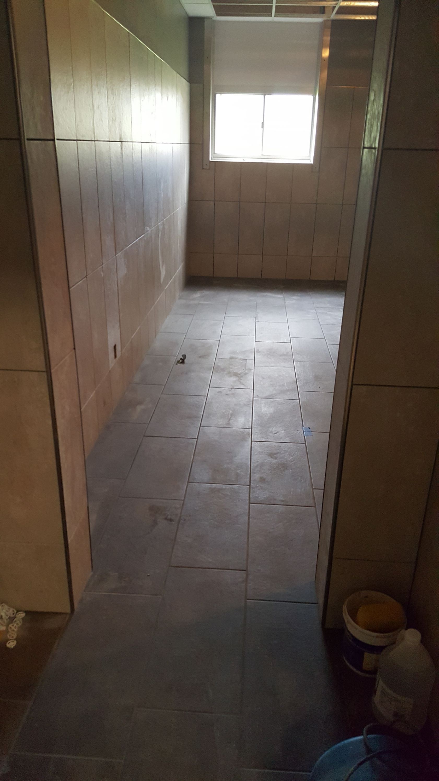 Narrow hallway, unfinished with exposed wall panels and dark floor tiles, leading to a window.