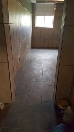 Narrow hallway, unfinished with exposed wall panels and dark floor tiles, leading to a window.