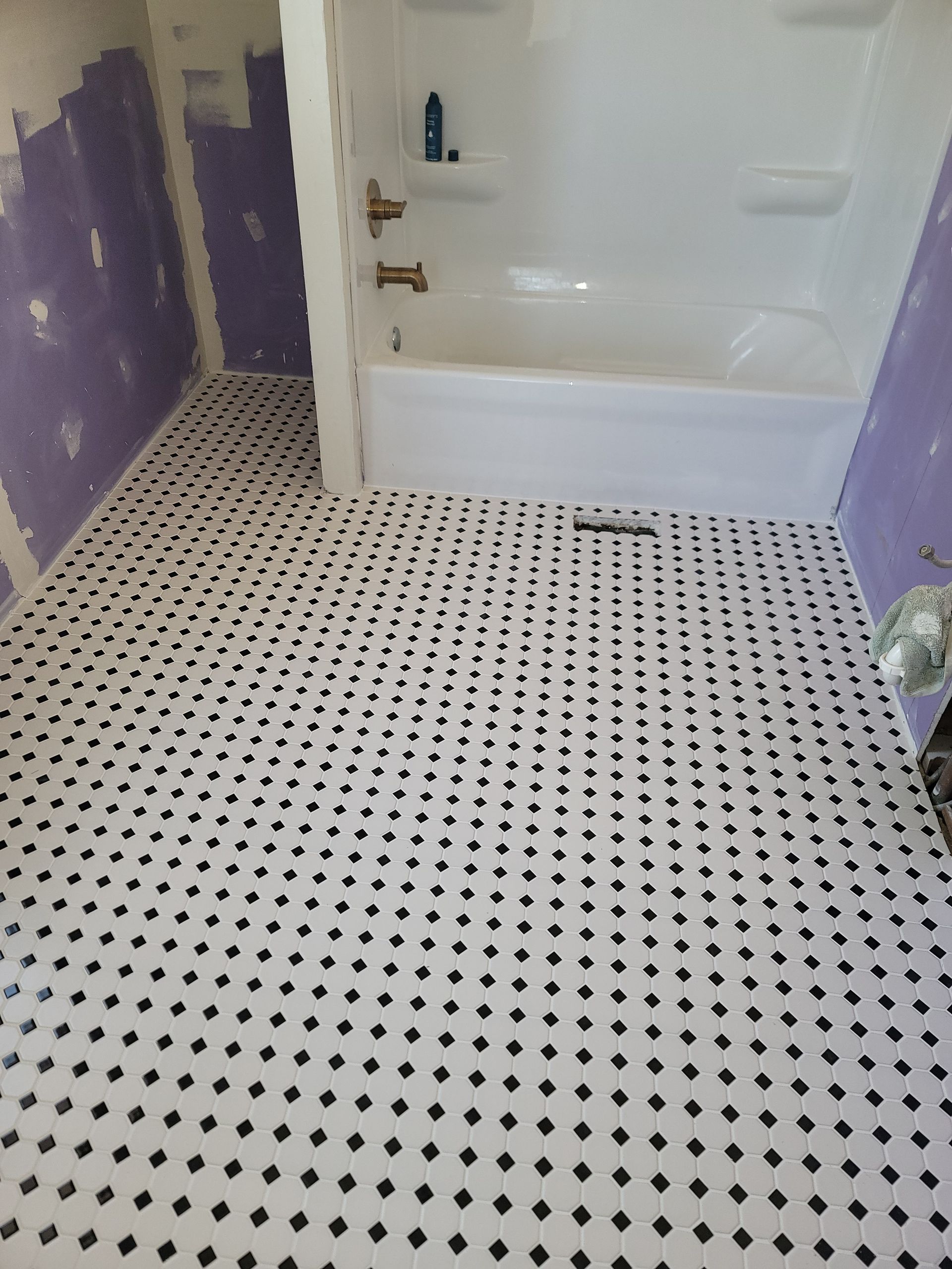 Bathroom floor with black and white tile, white bathtub, purple walls.