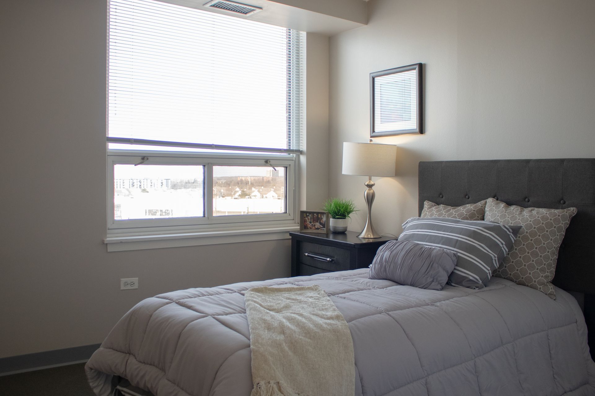 A bedroom with a bed , nightstand , lamp and window.