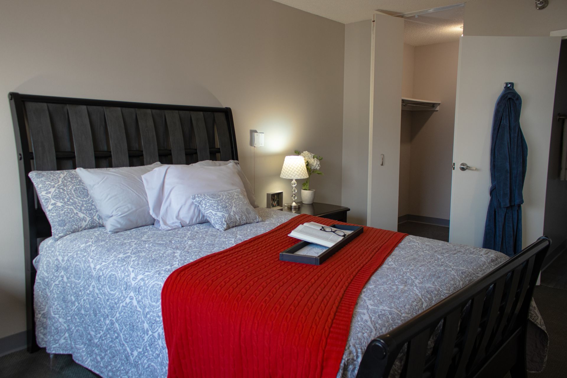 A bedroom with a bed , nightstand , lamp and closet.