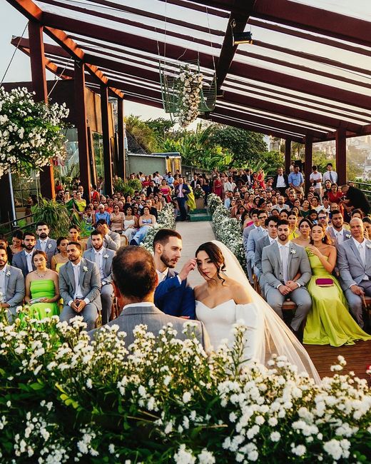 A bride and groom exchange vows at an outdoor altar while guests look on under a rustic wooden pergola.