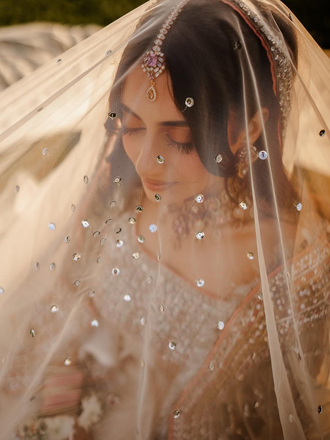 A person wearing a sheer, sequined veil over their head, adorned with a decorative headpiece on their forehead.
