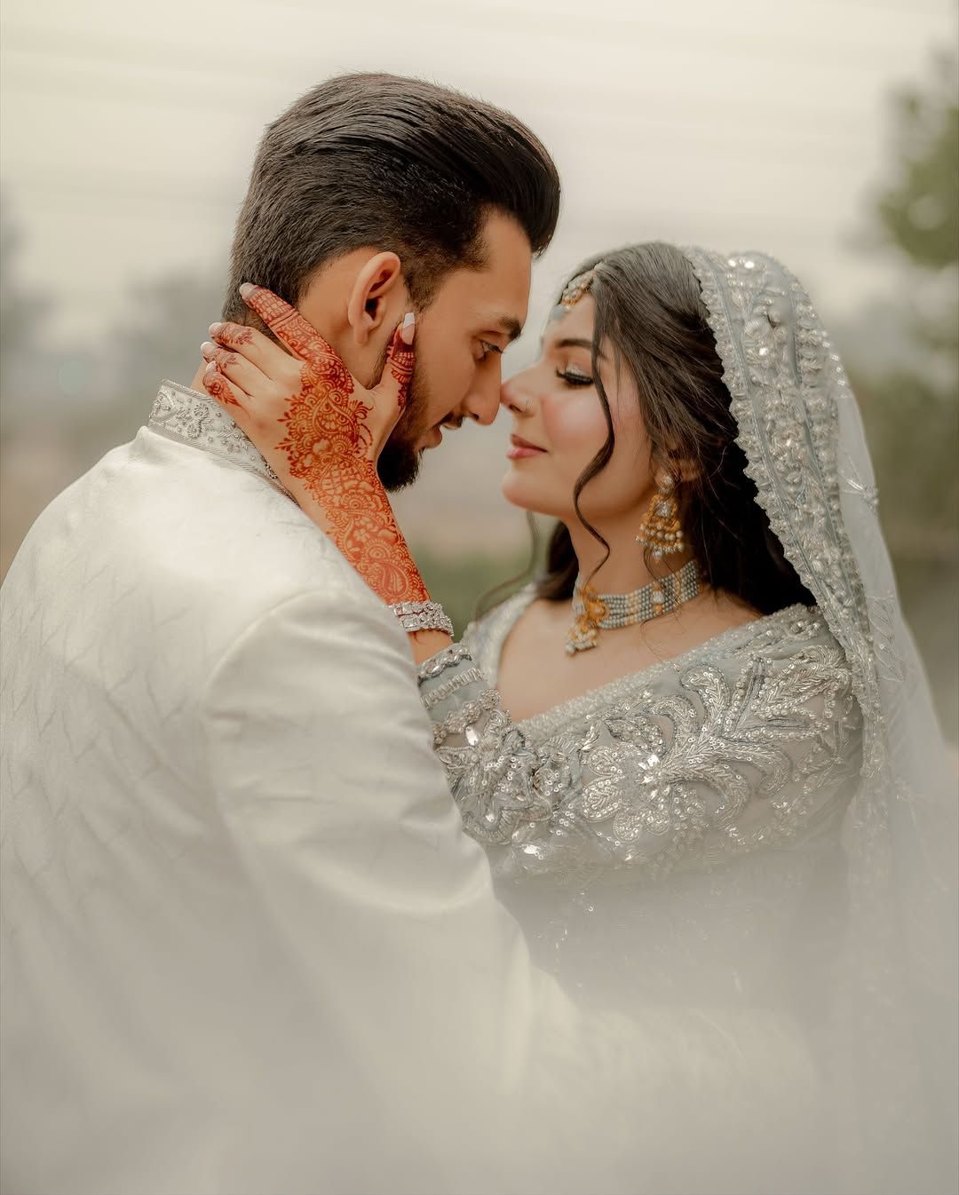 A couple in elegant white and silver traditional wedding attire shares an intimate, close-up moment.
