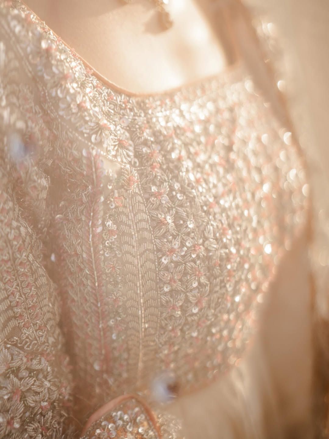 A close-up of a garment with intricate, shimmering beadwork and embroidery in soft, warm gold tones.