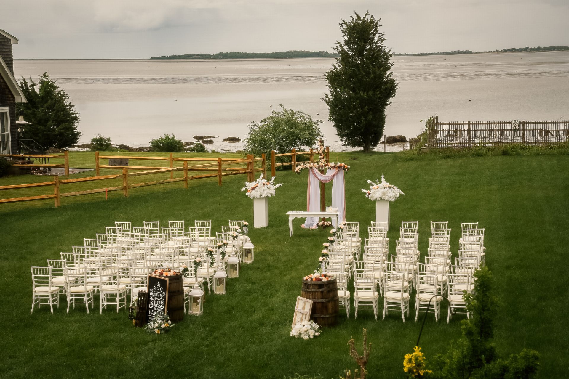 Outdoor wedding ceremony setup on a lawn overlooking a calm body of water with white chairs arranged around an altar.