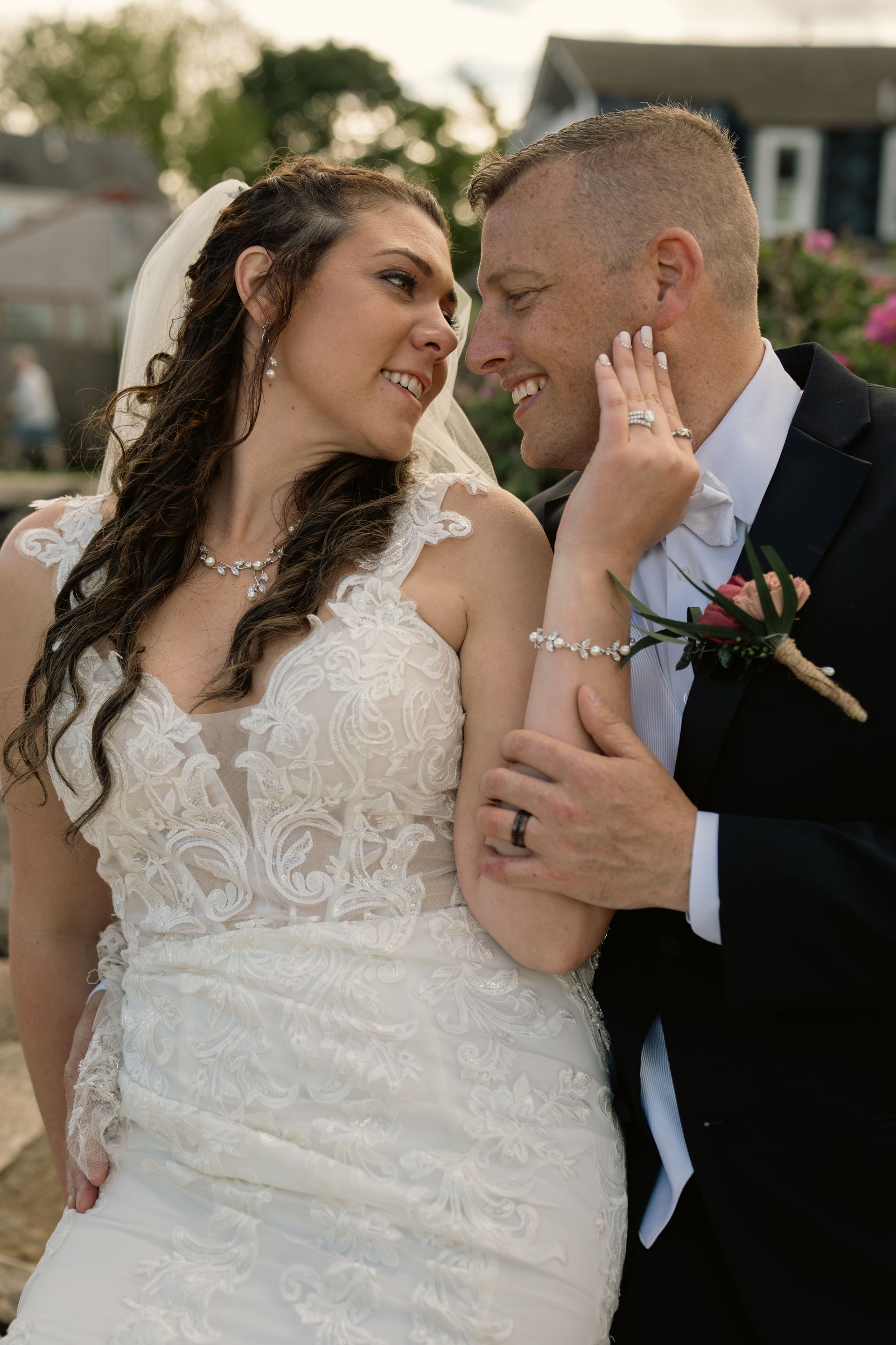 A bride and groom in wedding attire look at each other, the bride's hand gently touching the groom's face.